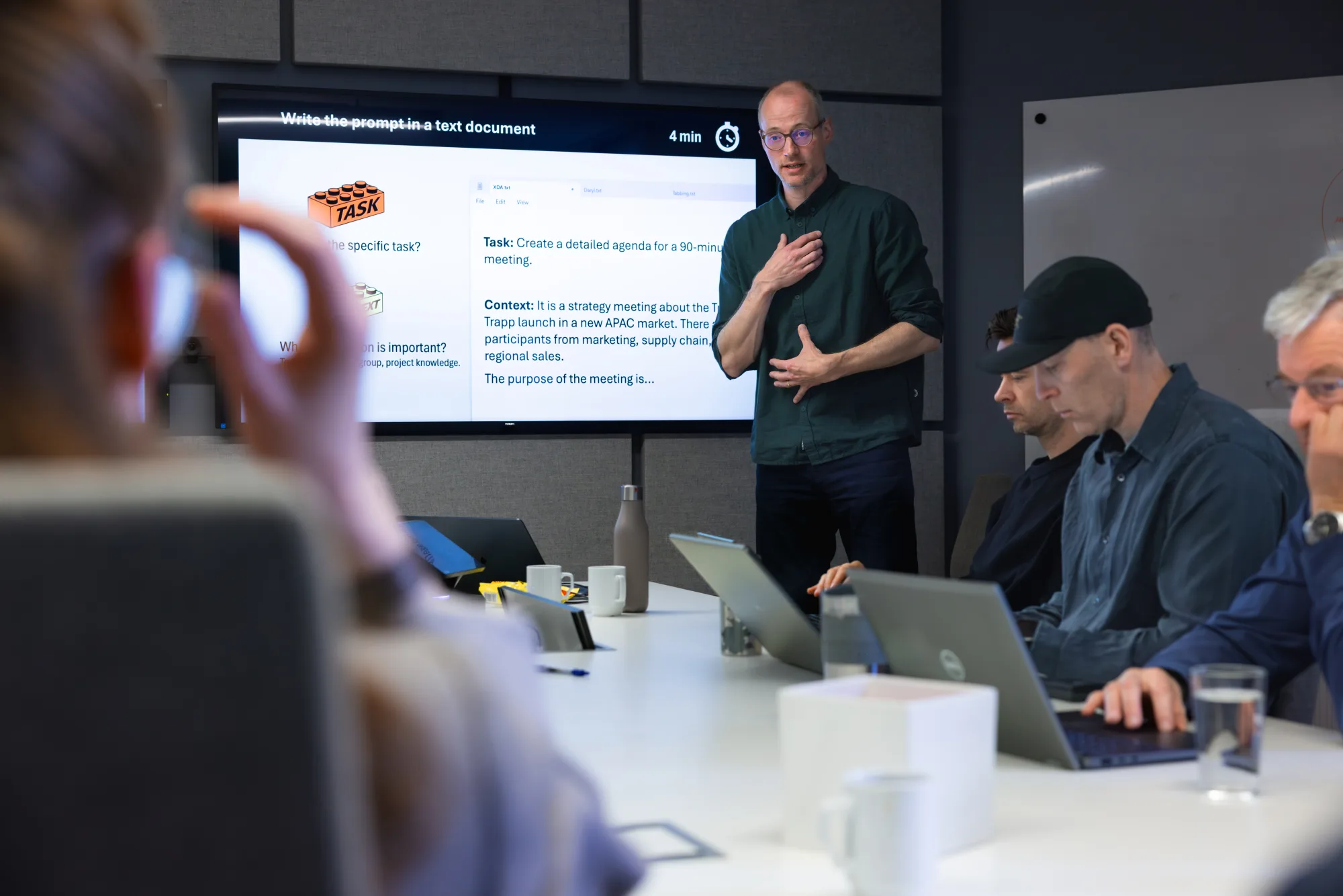 Work session at Stokke in Oslo: a trainer explains a prompting approach to a team with laptops